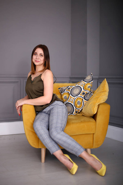 Stylish beautiful girl with a bob hairstyle sits in a yellow armchair - Φωτογραφία, εικόνα