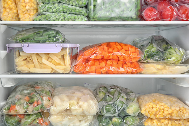 Plastic bags and containers with different frozen vegetables in refrigerator - Foto, Bild