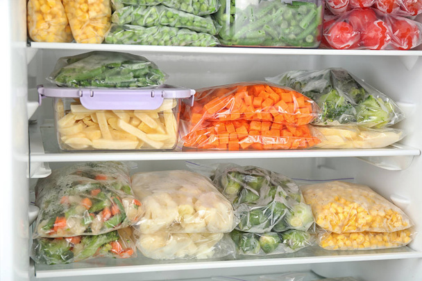 Plastic bags and containers with different frozen vegetables in refrigerator - Foto, Imagem