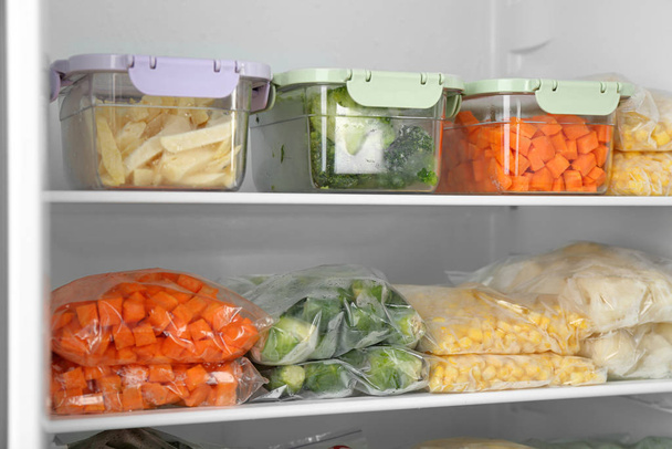 Plastic bags and containers with different frozen vegetables in refrigerator - 写真・画像