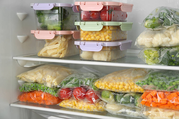 Plastic bags and containers with different frozen vegetables in refrigerator - Фото, изображение