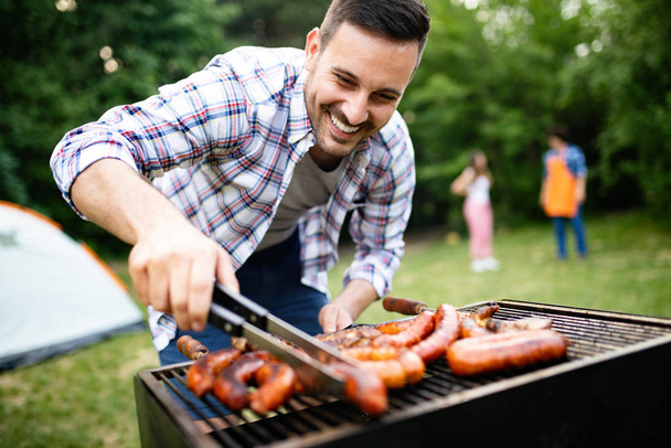 Leisure, food, people and holidays concept. Man cooking meat on barbecue grill at outdoor summer party - Foto, Imagen