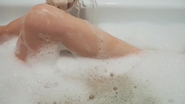 dívka smyslně omývá své štíhlé nohy žínkou v koupelně s mýdlovou pěnou - Záběry, video