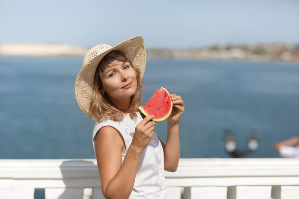 A woman in summer in a white blouse with a slice of watermelon in her hands - Фото, зображення