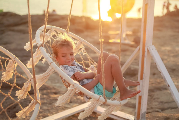 Un enfant au coucher du soleil monte dans une balançoire suspendue à l'extérieur
 - Photo, image