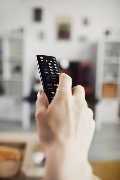 Close up of male hand holding TV remote against big screen television set, copy space - Photo, Image