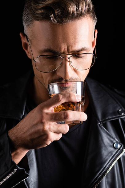 Handsome man in sunglasses drinking whiskey isolated on black  - Foto, Imagen