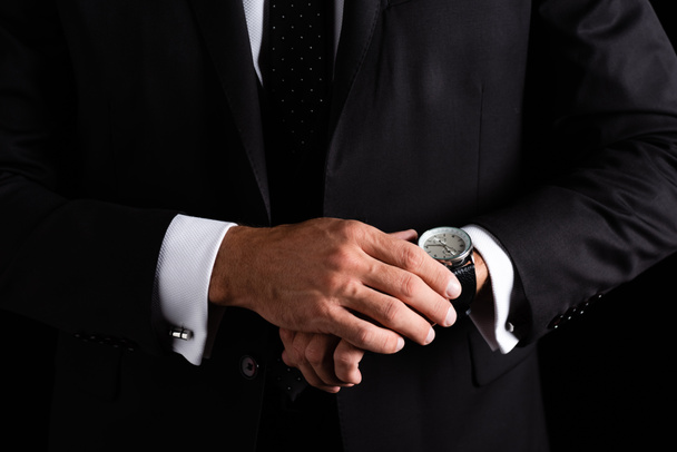 Cropped view of businessman in formal wear checking wristwatch isolated on black - Фото, изображение