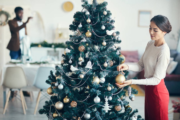 Vysokoúhlý portrét moderního páru připravujícího se na večeři doma, zaměření na mladou ženu zdobící vánoční stromek v popředí, kopírovací prostor - Fotografie, Obrázek