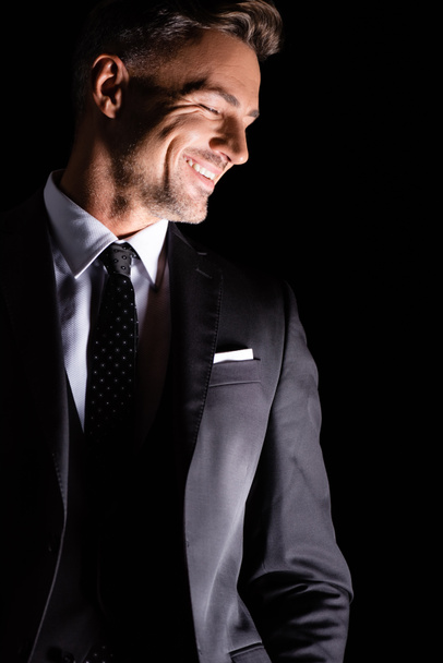 Businessman in formal wear looking down and smiling isolated on black  - Photo, Image