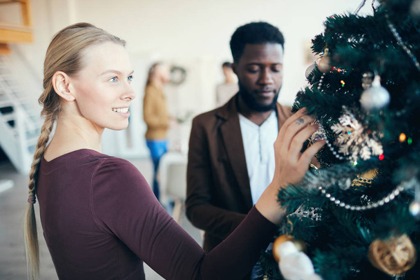 Taille nach oben Portrait der schönen jungen Frau beim Betrachten von Dekorationen am Weihnachtsbaum während des Festbanketts, Kopierraum - Foto, Bild