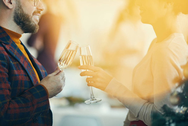 Closeup of adult couple drinking champagne and talking during Christmas banquet, golden lens flare overlay - 写真・画像