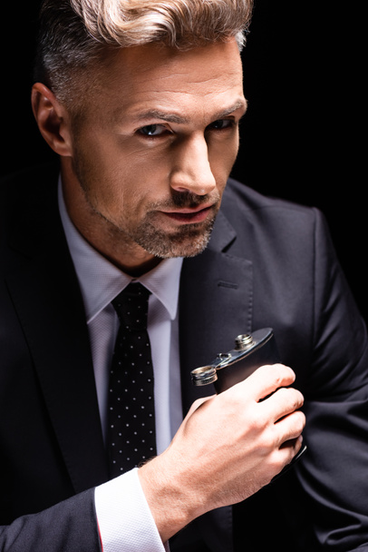 Hombre de negocios confiado sosteniendo el frasco y mirando a la cámara aislada en negro
  - Foto, Imagen