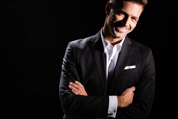 Smiling businessman with crossed arms looking at camera isolated on black  - Foto, Imagem