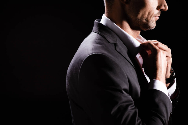 Gekropte weergave van zakenman knopen tot shirt geïsoleerd op zwart - Foto, afbeelding