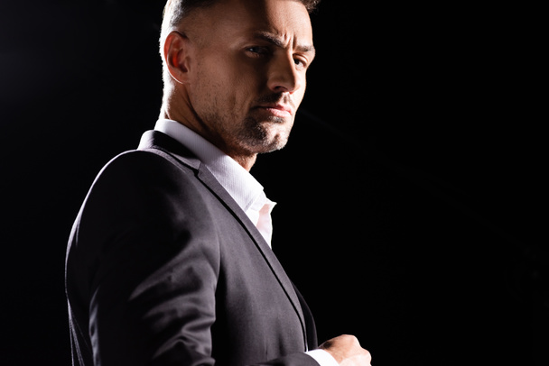 Side view of confident businessman looking at camera isolated on black  - Foto, afbeelding