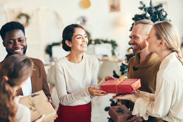 Група елегантних молодих людей, які обмінюються подарунками та весело посміхаються під час різдвяної вечірки, копіюють простір
 - Фото, зображення