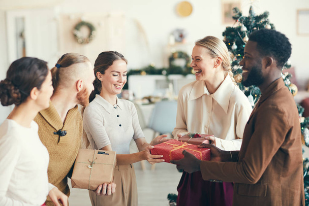 Waist up portrait of cheerful young people exchanging presents during Christmas party in cozy interior, copy space - Photo, image