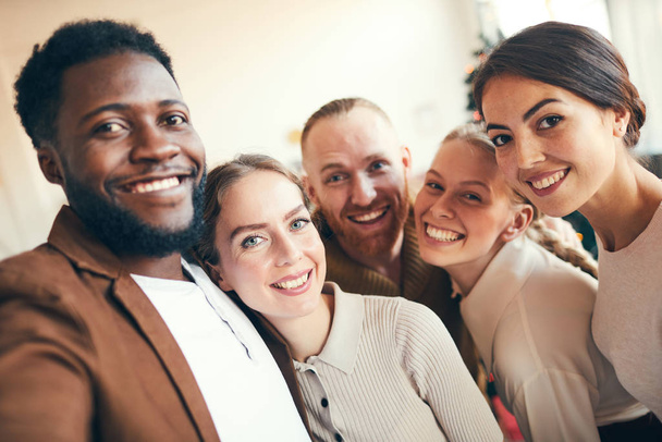 Grupo multiétnico de personas adultas elegantes sonriendo a la cámara mientras toman fotos de selfies durante la fiesta de Navidad
 - Foto, Imagen