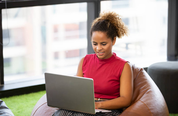 Foto de la cabeza de la sonriente afroamericana millennial femenino utilizando el ordenador portátil
 - Foto, imagen