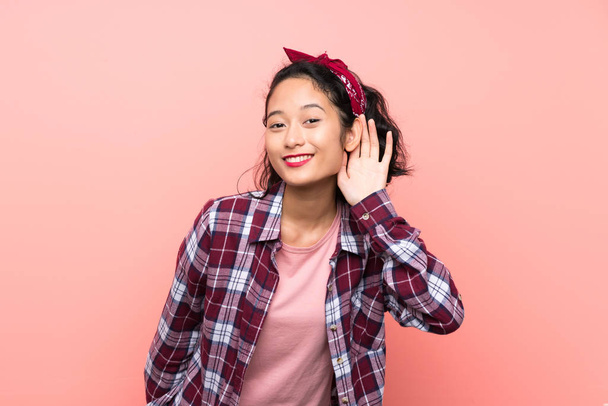 Asiatique jeune femme sur fond rose isolé écoute quelque chose en mettant la main sur l'oreille
 - Photo, image