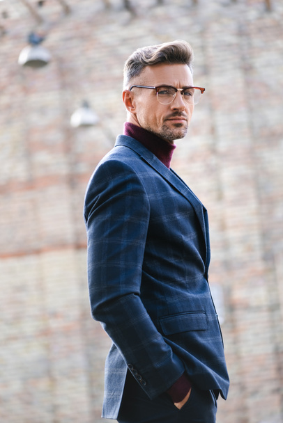 Side view of stylish businessman looking at camera on urban street - Photo, Image