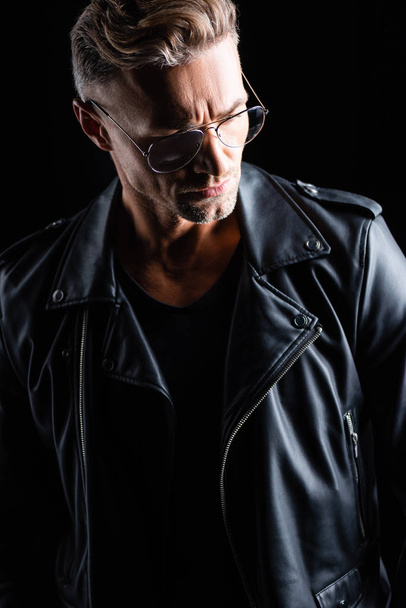 Handsome man in leather jacket looking down isolated on black - Foto, Bild