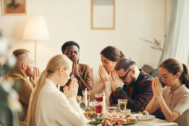 Grupo multi-étnico de pessoas dizendo graça à mesa de jantar durante o banquete de Natal com amigos e familiares
 - Foto, Imagem