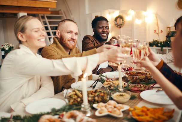 Grupo multiétnico de personas levantando vasos mientras celebran la Navidad con amigos y familiares sentados en la hermosa mesa de la cena
 - Foto, Imagen