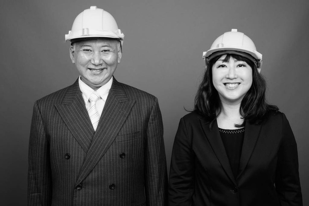 Mature Asian businessman and mature Asian businesswoman wearing hardhat together - 写真・画像