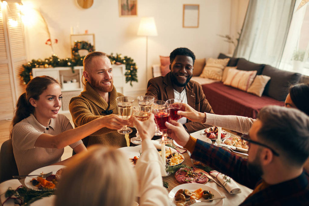 Grupo multiétnico de jóvenes tintineando copas de champán mientras disfrutan de la cena de Navidad en casa, espacio para copiar
 - Foto, Imagen