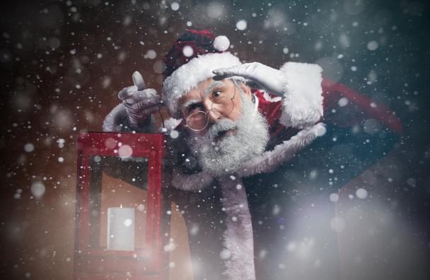 Cintura até retrato de conto de fadas Santa segurando lanterna andando através de tempestade de neve à noite, espaço cópia
 - Foto, Imagem