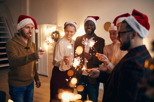 Grupo multiétnico de personas con luces brillantes mientras disfrutan de la celebración de Navidad con amigos y familiares
 - Foto, Imagen