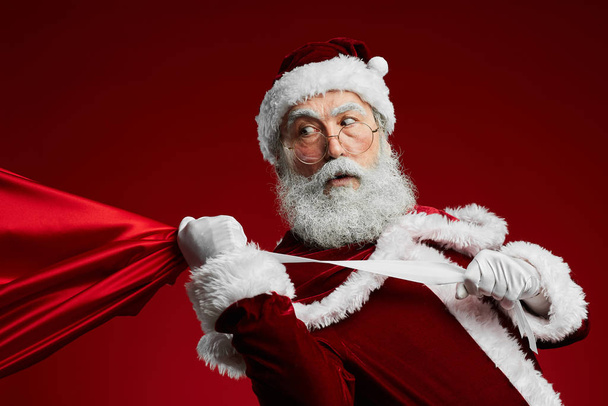 Vyötärö ylös muotokuva Santa Claus hinaus laukku joululahjoja yli punainen tausta, kopioi tilaa
 - Valokuva, kuva