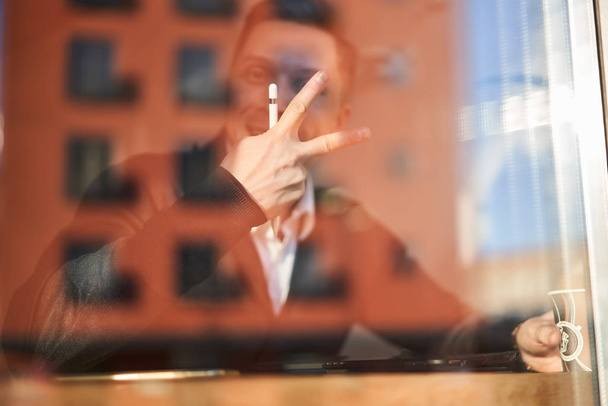 Male businessman with phone and tablet sitting in cafe, building reflection - Foto, afbeelding