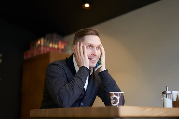 Smiling businessman with phone in hands sitting at table - Valokuva, kuva