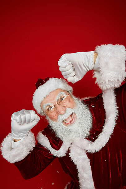 Portrait grand angle du Père Noël classique dansant joyeusement tout en se tenant debout sur fond rouge en studio, espace de copie
 - Photo, image