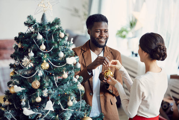 Retrato de alto ângulo de casal sorrindo decorando árvore de Natal juntos em pé na elegante sala de estar, espaço de cópia
 - Foto, Imagem