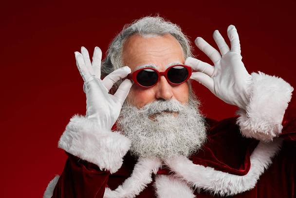 Голова и плечи портрет фанки Санты в солнцезащитных очках, готовый насладиться рождественской вечеринкой на красном фоне
 - Фото, изображение
