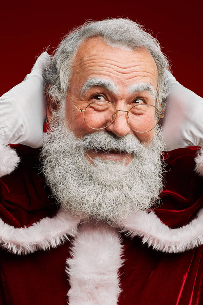 Kopf und Schultern Porträt eines lächelnden Weihnachtsmannes, der vor rotem Hintergrund wegschaut - Foto, Bild