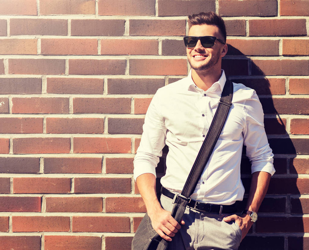 young man in sunglasses with bag over brickwall - Foto, Imagen