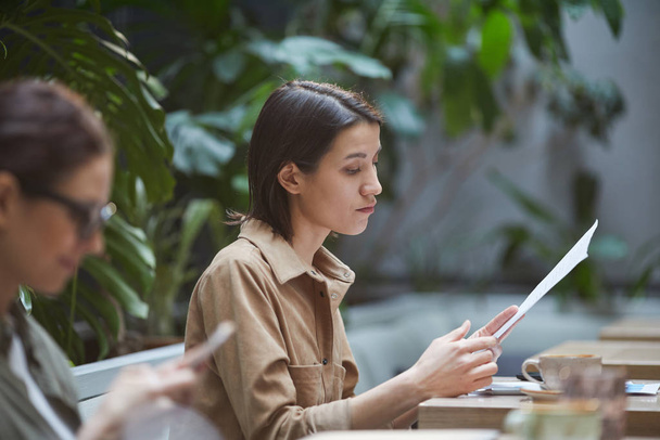 Side view portrait of young businesswoman reading documents while working in outdoor cafe, copy space - Photo, image