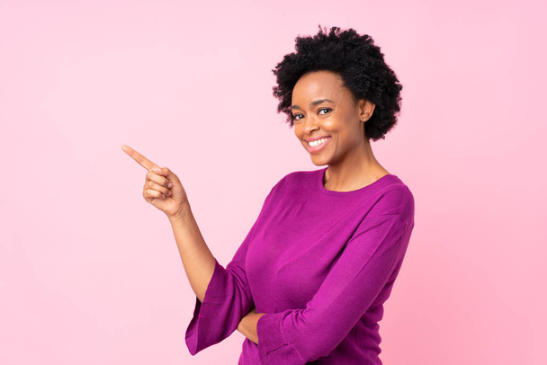 アフリカ系アメリカ人女性がピンクの背景色を指差して - 写真・画像