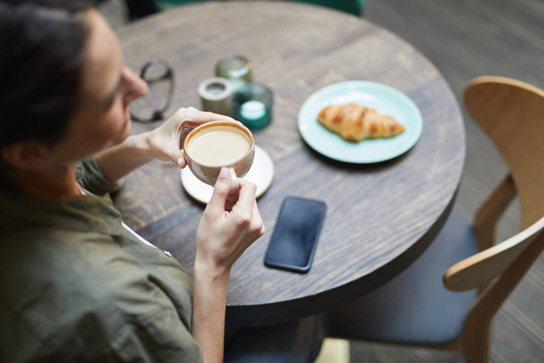 Vista de ángulo alto de la joven sonriente sosteniendo una taza de café con leche fresca sobre una mesa de madera en un café francés, espacio para copiar
 - Foto, Imagen