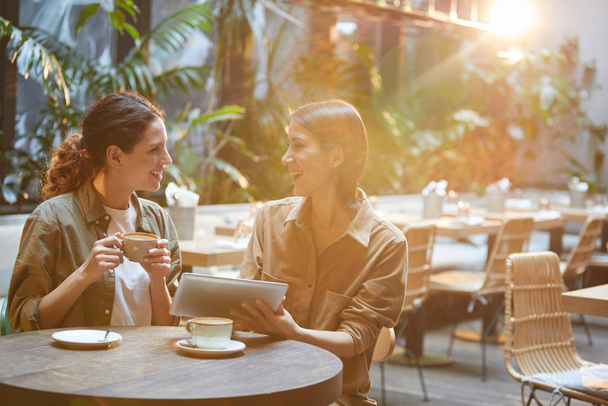 Portrait of two contemporary women chatting cheerfully while enjoying meeting in sunlit care terrace, copy space - Foto, Bild
