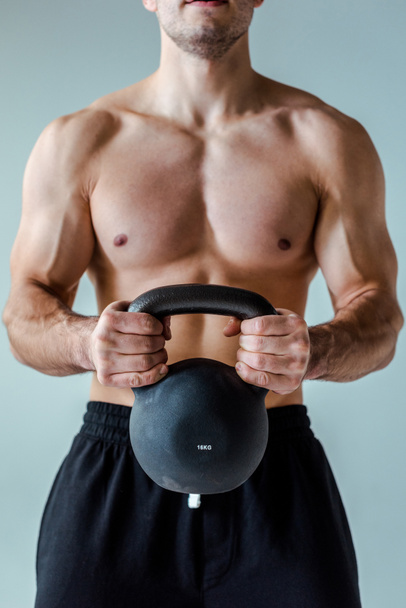částečný pohled na sexy svalový kulturista s holým trupem cvičení s kettlebell izolované na šedé - Fotografie, Obrázek