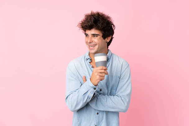 junger kaukasischer Mann vor isoliertem rosa Hintergrund mit Kaffee zum Mitnehmen - Foto, Bild