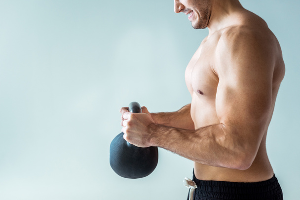 partial view of sexy muscular bodybuilder with bare torso exercising with kettlebell isolated on grey - Foto, Bild