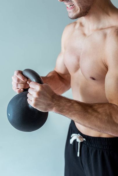 partial view of sexy muscular bodybuilder with bare torso exercising with kettlebell isolated on grey - Foto, immagini