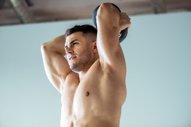 low angle view of sexy muscular bodybuilder with bare torso exercising with kettlebell - Fotografie, Obrázek